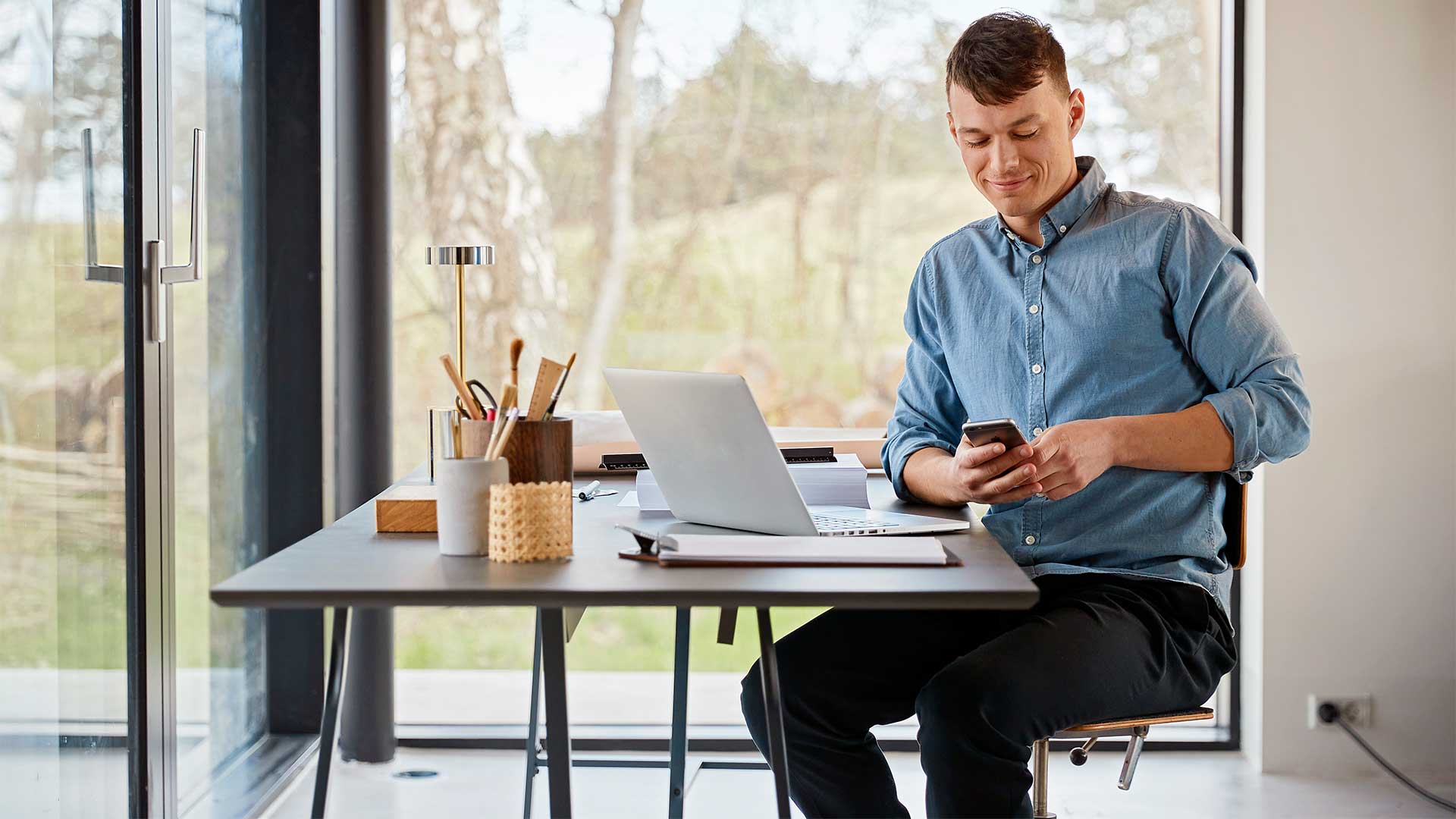 Mand sidder ved skrivebord med pc og mobil. Han undersøger hvilken trådløs router er den bedste router til fibernet.