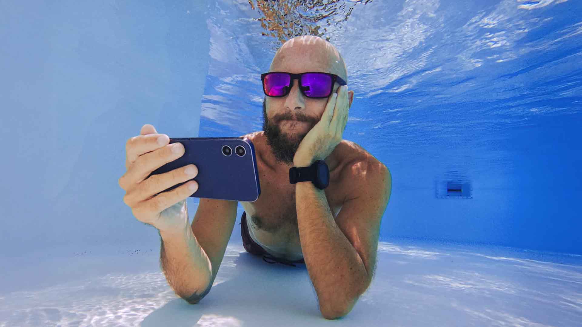 Mand streamer på mobil under vandet i swimmingpool. Han har taget sin Allente tv-pakke med på ferie. Hos EWII får han 20 % rabat på streaming tv-pakker.